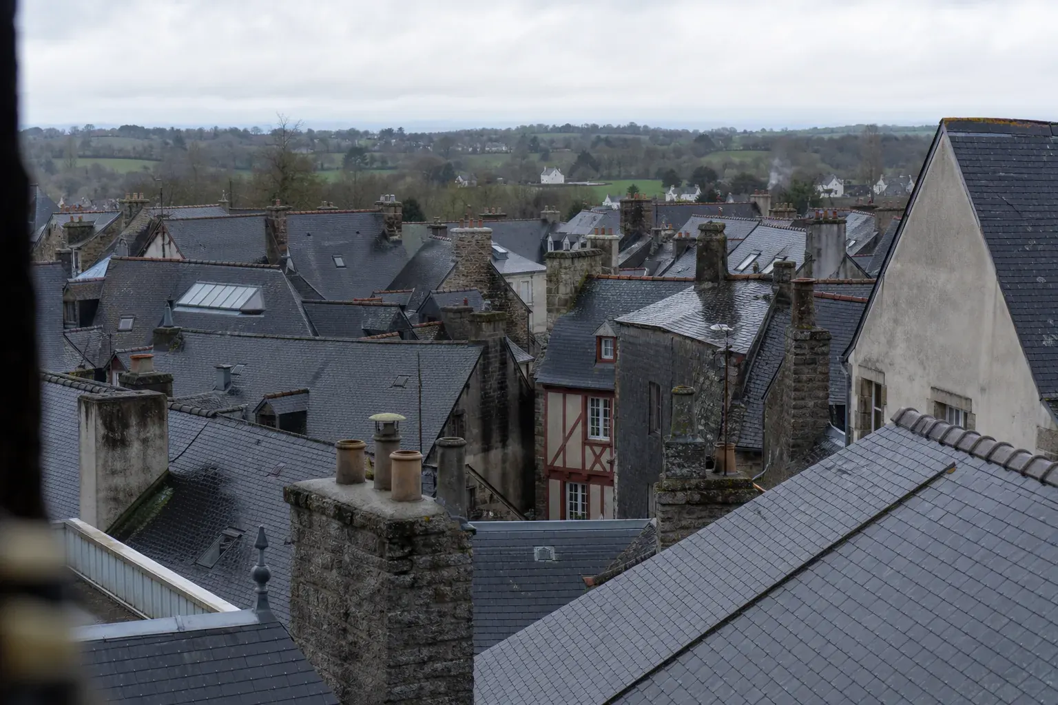 Vue large sur les toits d’ardoise d’une ville bretonne depuis une fenêtre haute, souches en granit et ciel gris