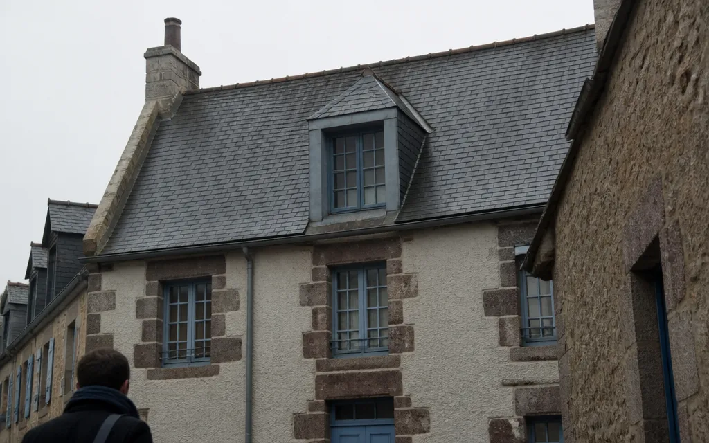 Lucarne dans un versant d’ardoise, avec son propre petit toit et ses joues en zinc, inscrite dans la longueur du pan